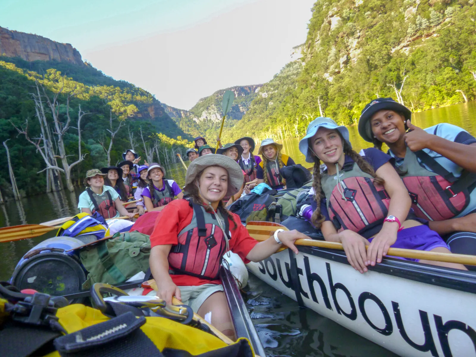 Students paddling Southbound canoes on a river between sandstone cliffs
