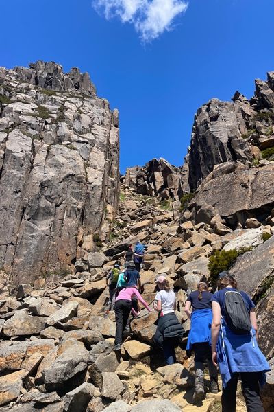 Students scrambling up a rocky ridgeline together under a clear blue sky