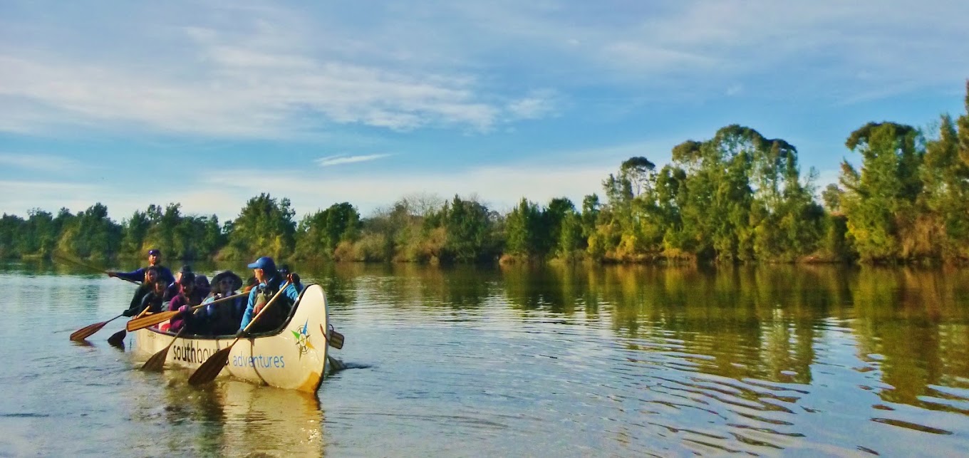 Team canoeing a wide river at sunrise on a Gold journey